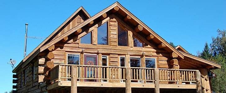 Wooden log cabin with a front porch and peaked roof under a clear blue sky