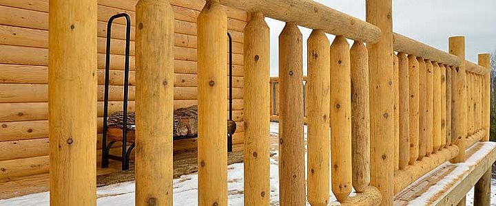 Wooden log railing along a snow-covered outdoor walkway on a rustic deck