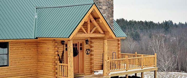 Wooden cabin with a green roof and deck overlooking a snowy forest