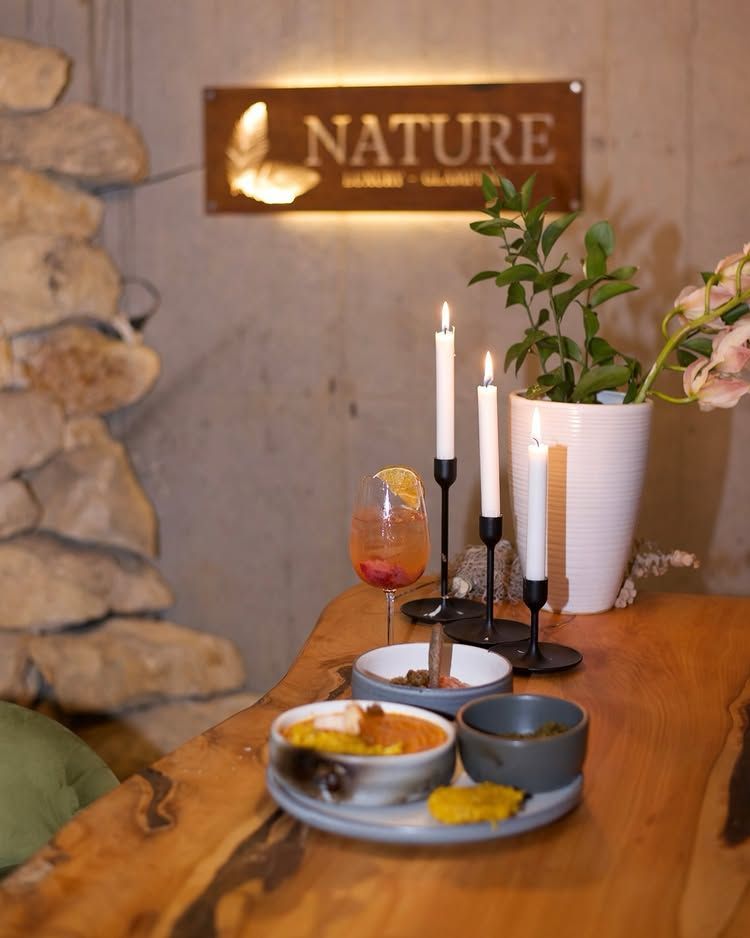 A dimly lit table with appetizers, a cocktail, and three candles, set before a wall sign reading 