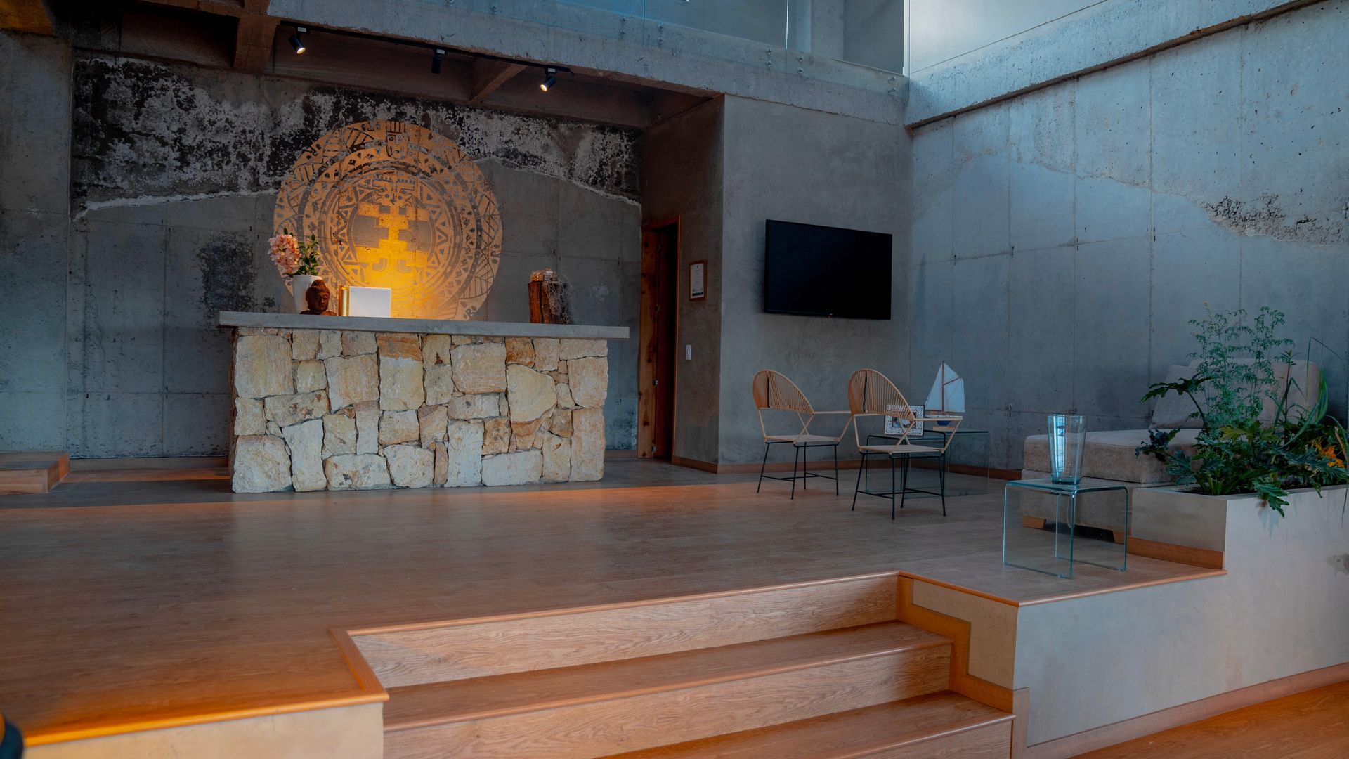 A minimalist hotel lobby featuring a stone reception desk, textured concrete walls, and a large circular mural backdrop.