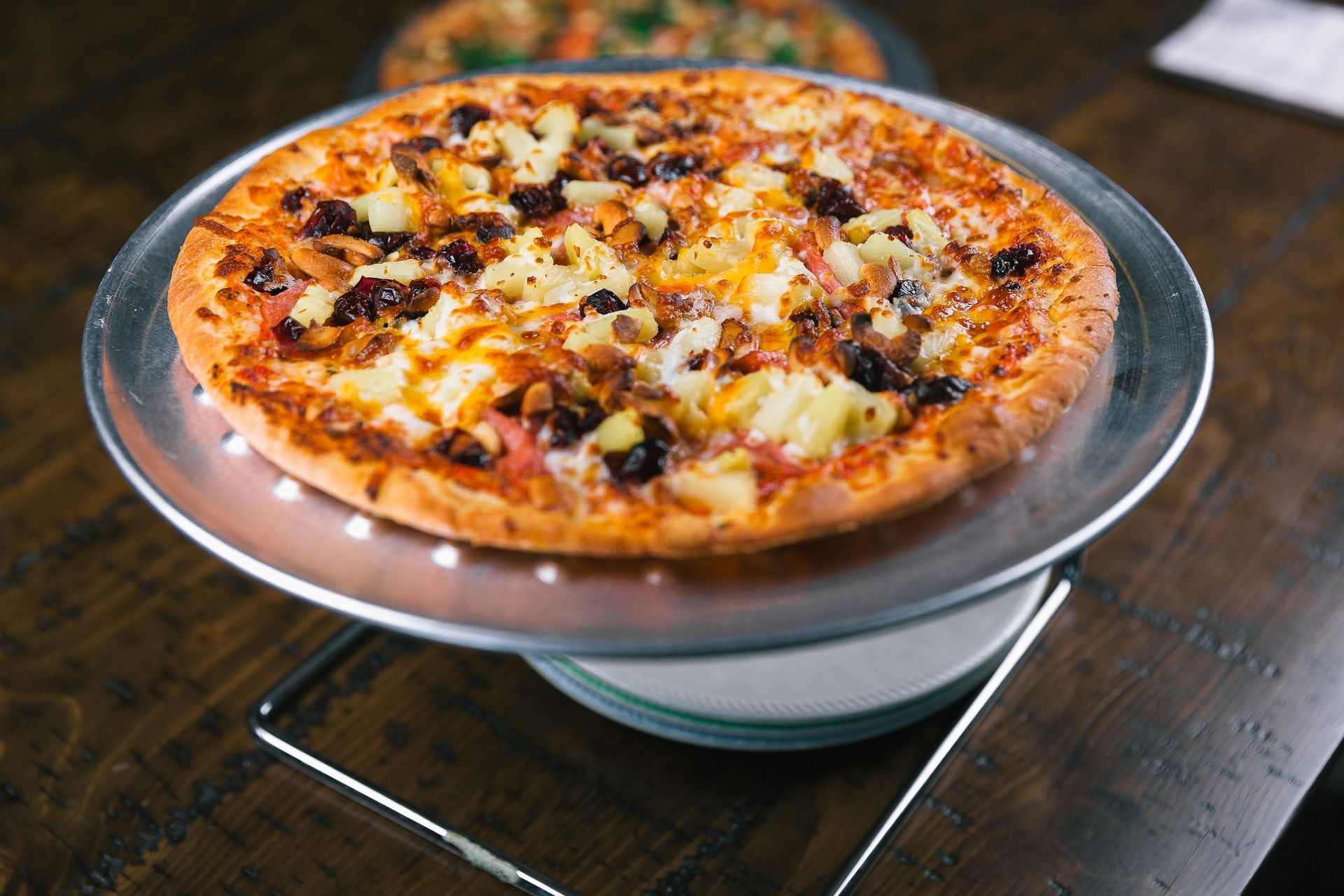 Cheese and vegetable pizza on a raised stand over a dark wooden table