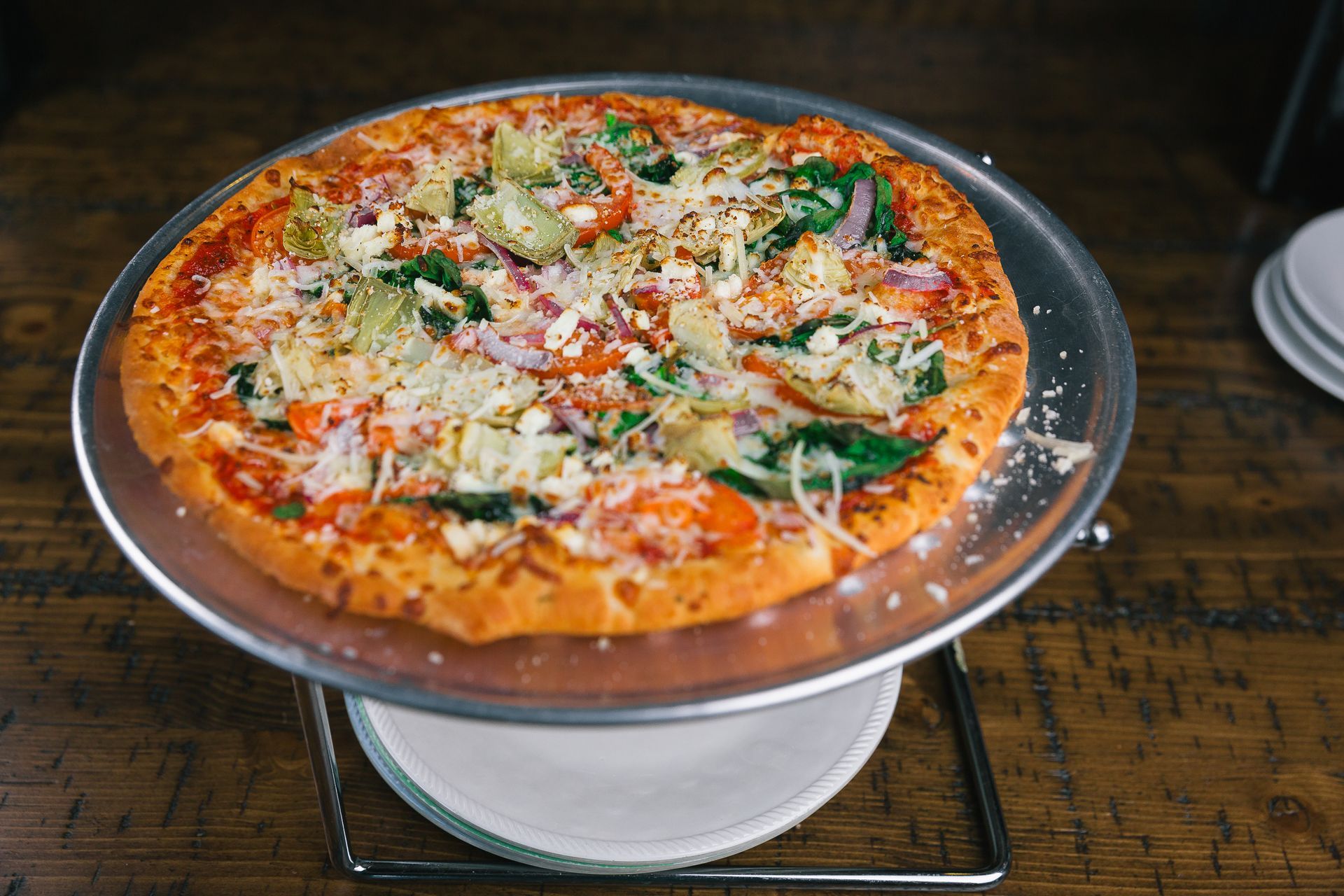 Pizza on a raised stand, topped with basil and grated cheese, on a rustic wooden table.