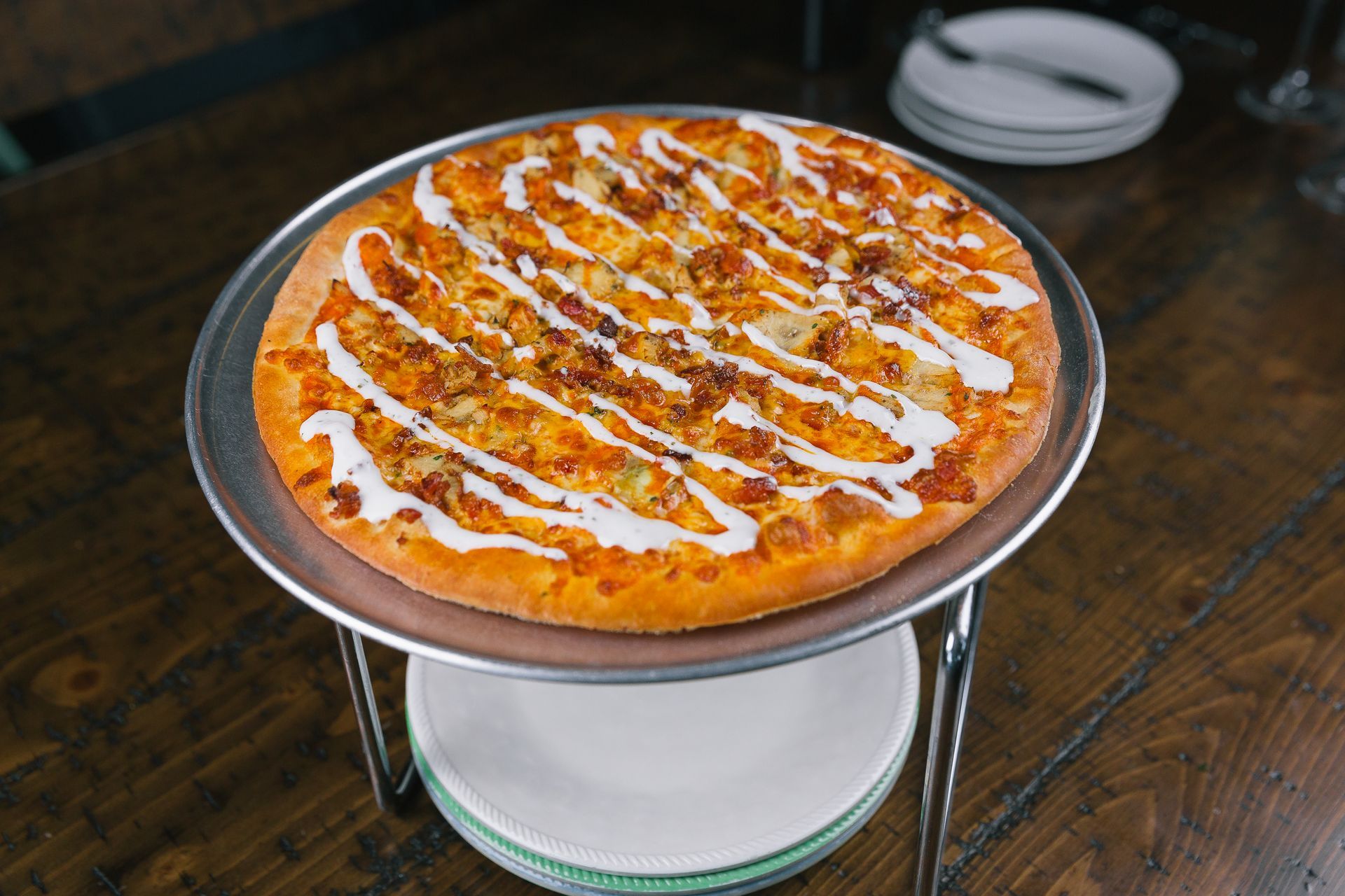 Round pizza topped with white sauce drizzle on a metal stand over a wooden table