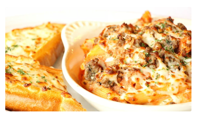 Cheesy baked pasta in a white dish with toasted bread slices on the side
