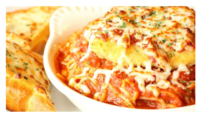 Baked pasta in a white dish with melted cheese and tomato sauce, served with garlic bread