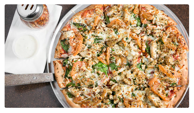 Shrimp and herb pizza on a metal tray beside a cup of dipping sauce