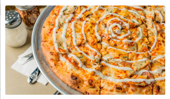Sausage pizza with white sauce swirled on top, on a metal tray with spices nearby