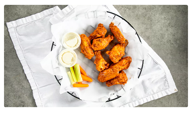 Buffalo chicken tenders on a white plate with celery, carrot sticks, and dipping sauce on a white cloth