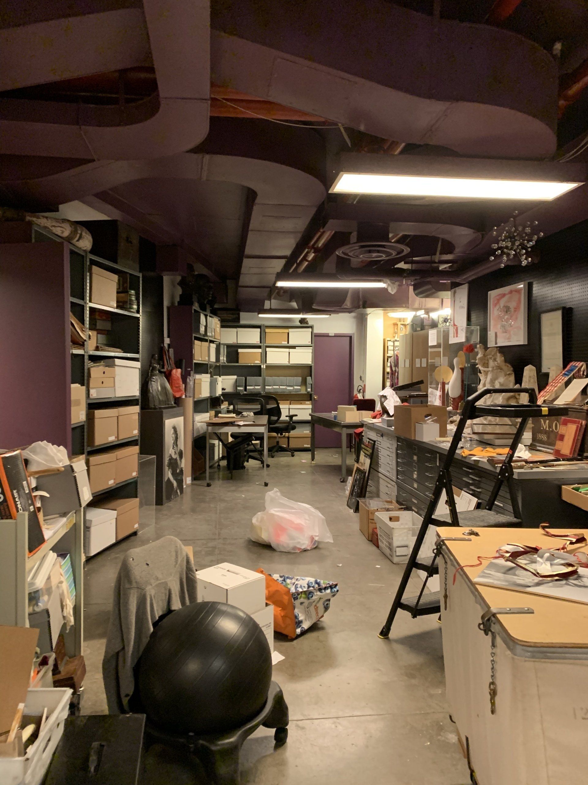 Cluttered art studio with shelves, tables, and storage. Purple walls and ceilings.