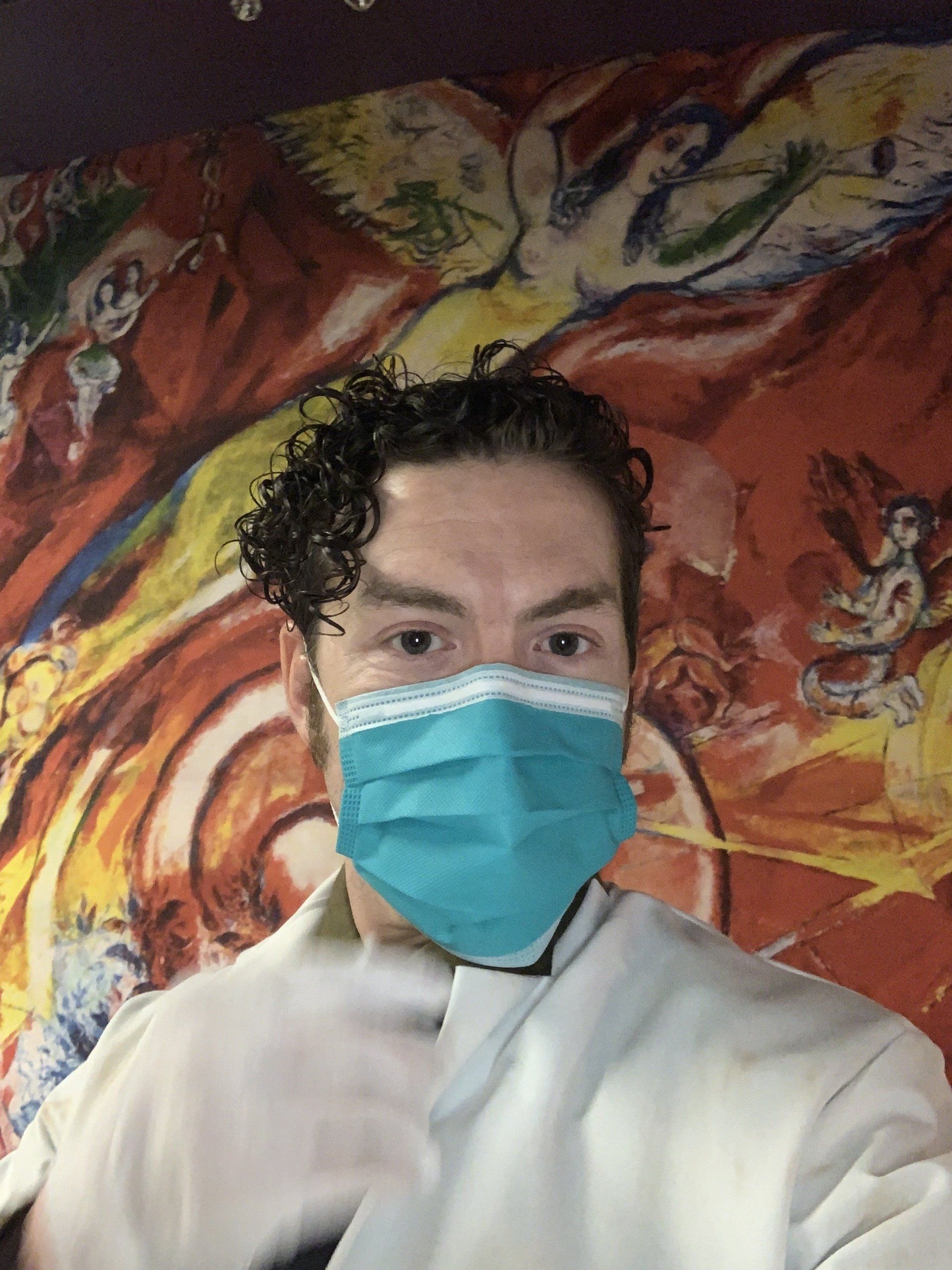 Person in a mask and gloves in front of a colorful mural.