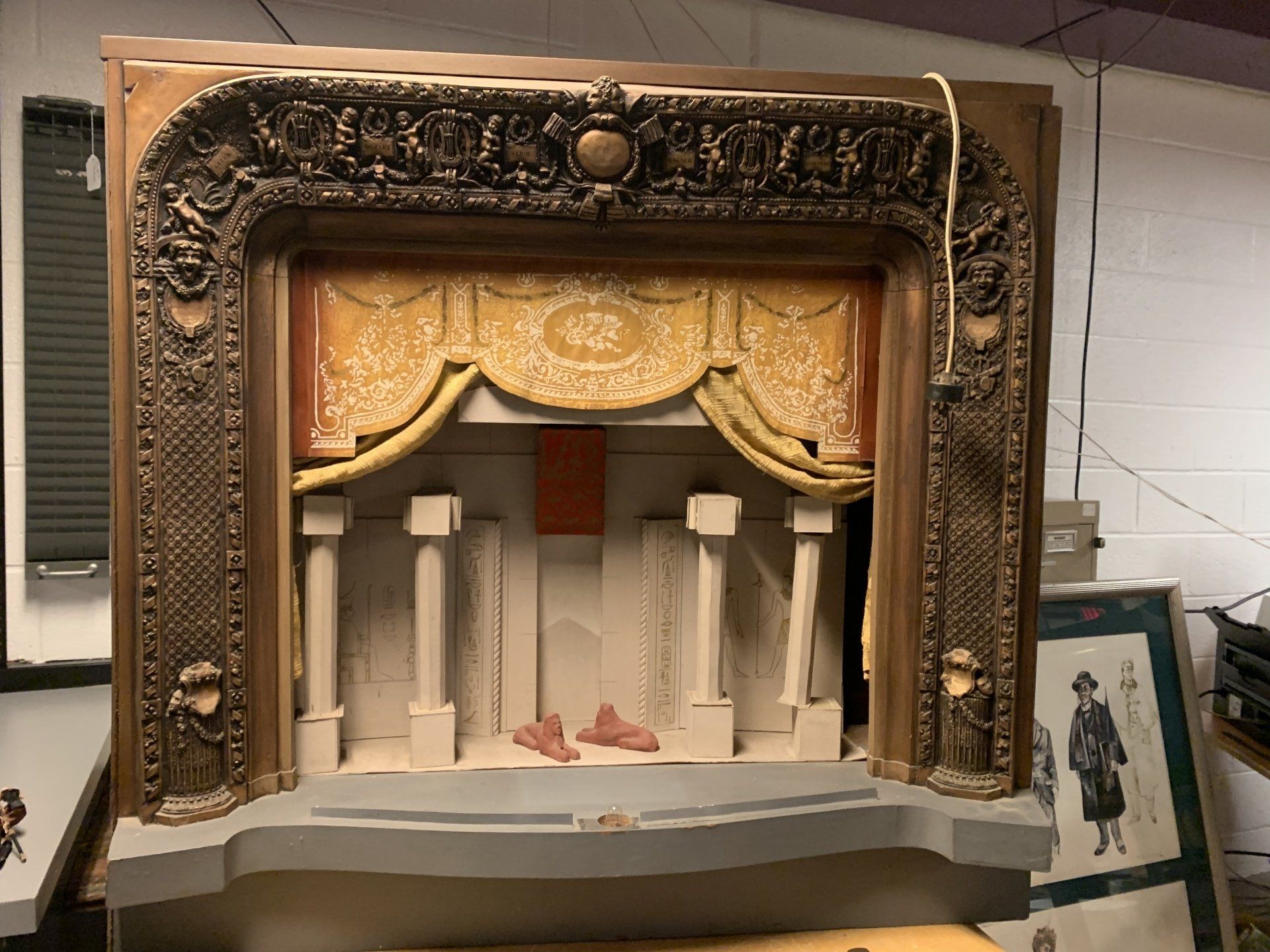 Miniature stage with gold curtains and decorative frame. White pillars and stage floor.