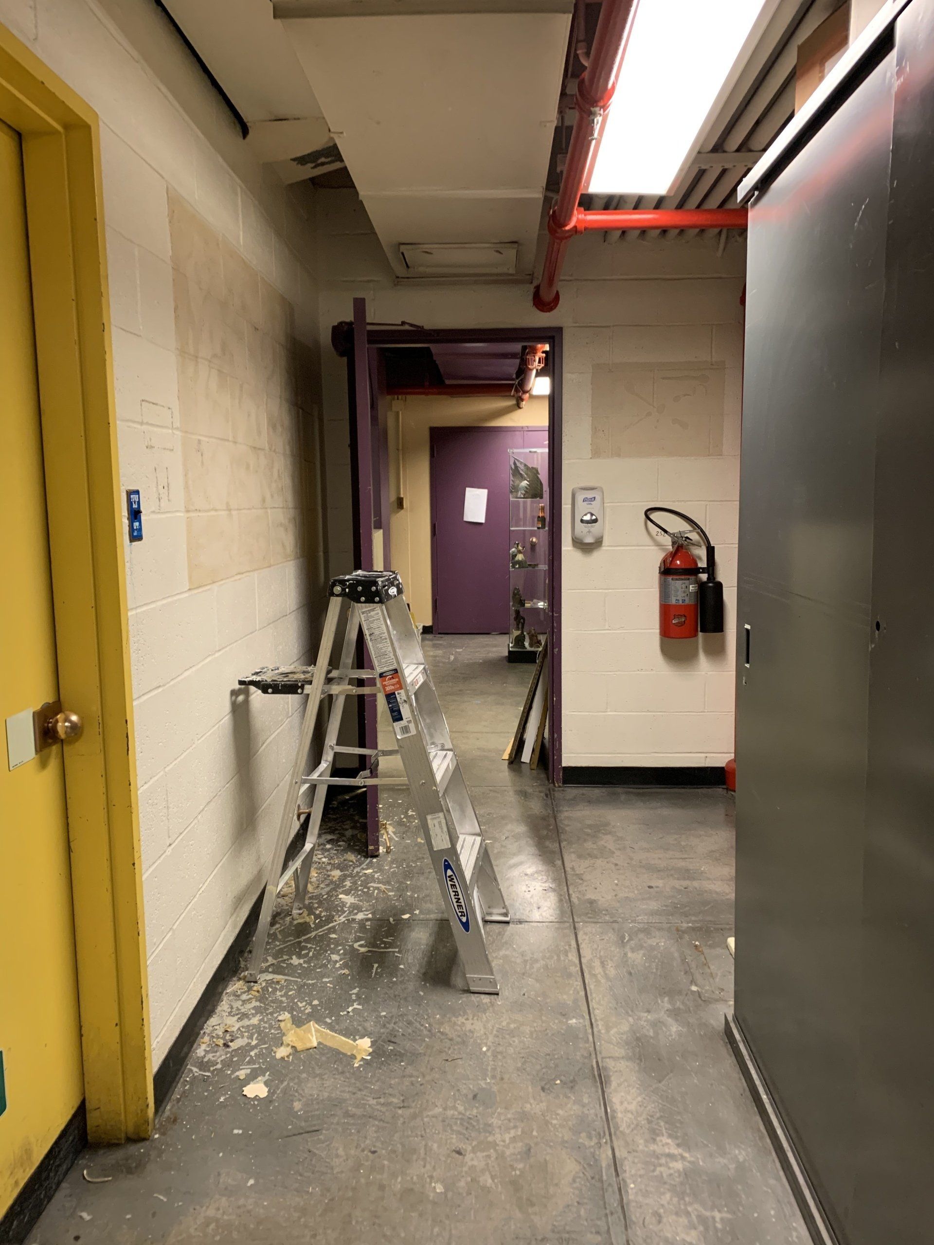 Hallway with ladder, debris on floor, open doorway, yellow and purple doors.
