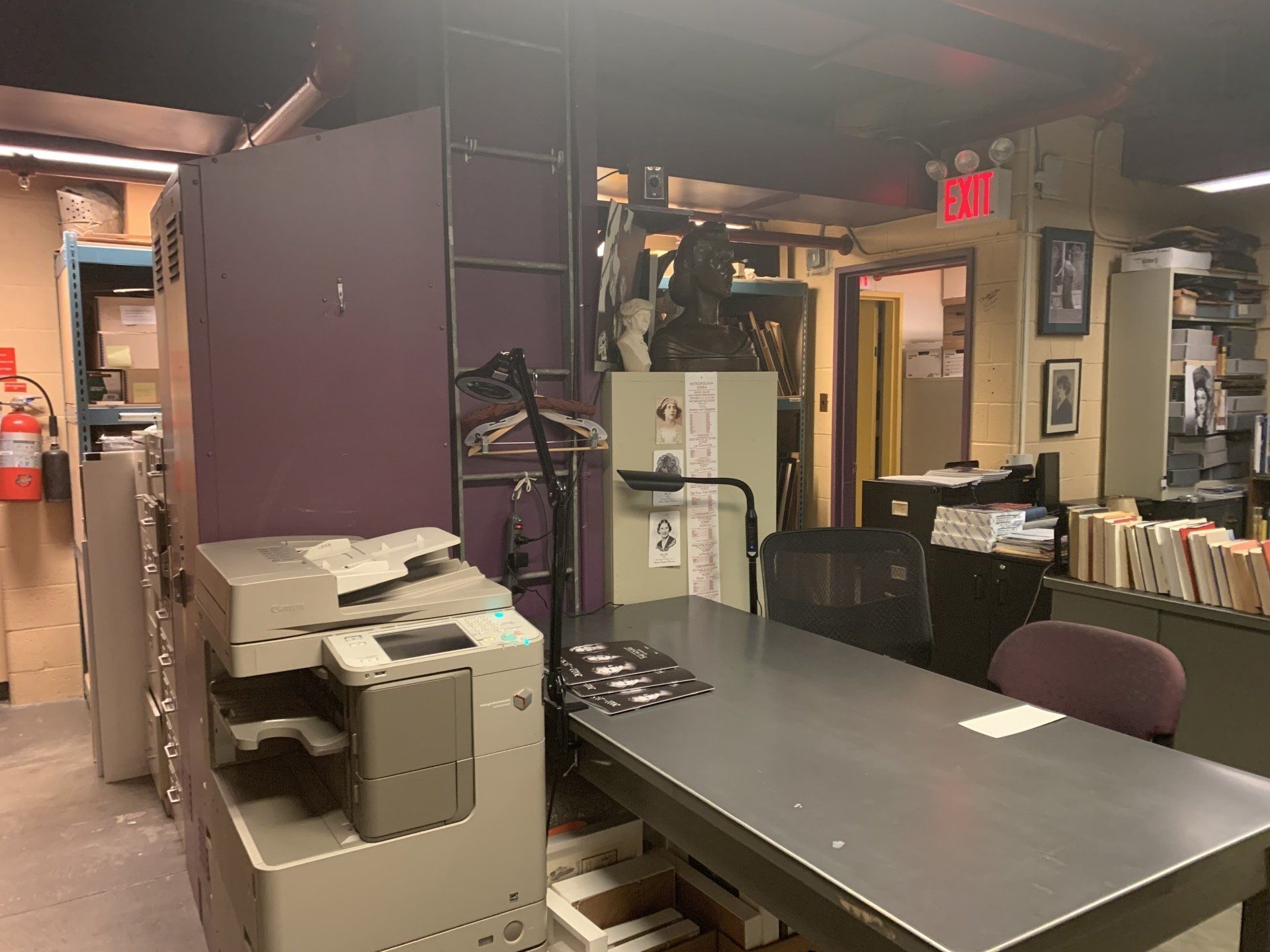 Office with printer, desk, and exit sign. Purple cabinet and a fire extinguisher are visible.
