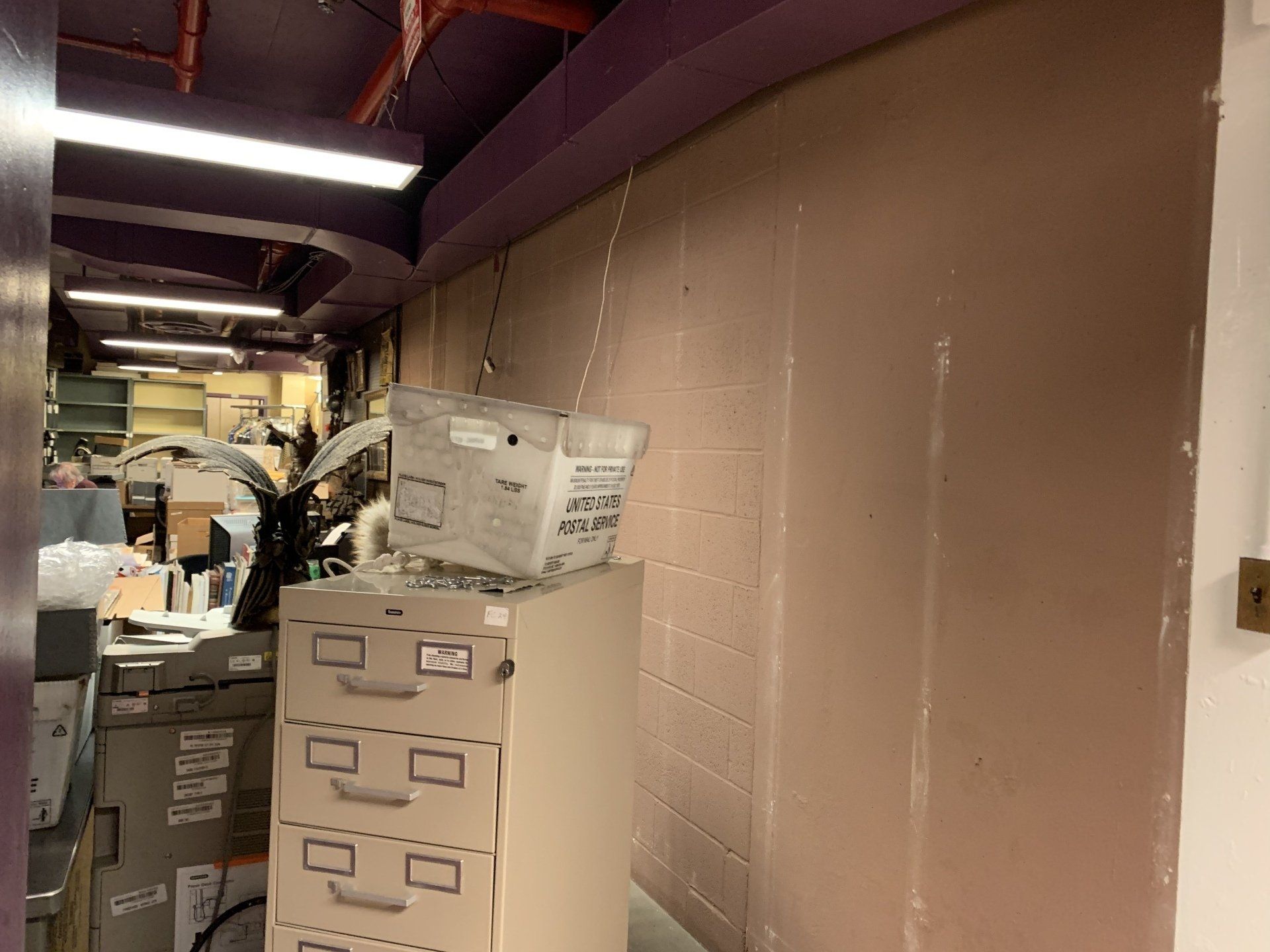 Filing cabinet with a box on top, a wall, and the edge of a room.