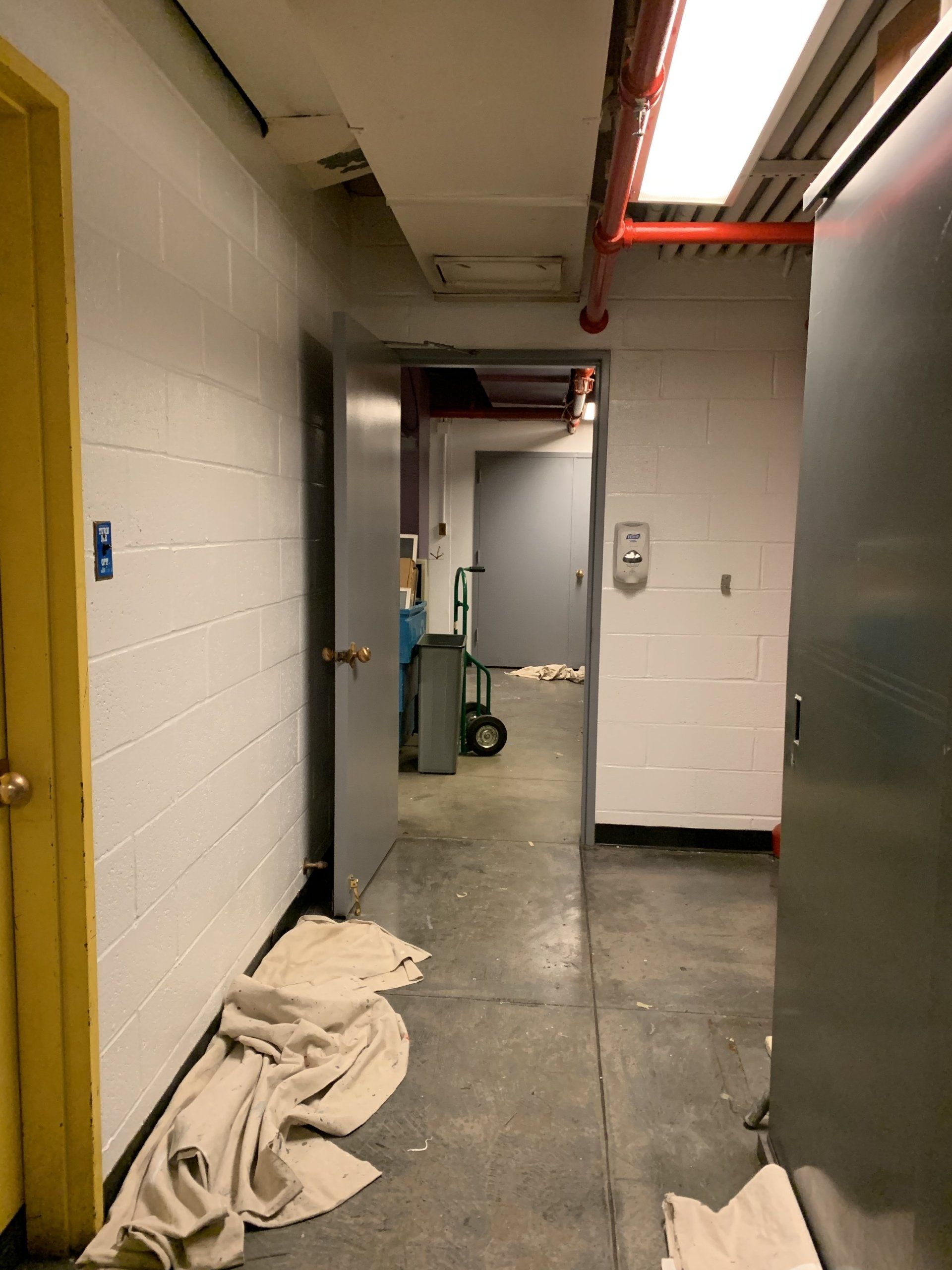 Narrow, institutional hallway with several doors. A cart and debris sit in the distance.