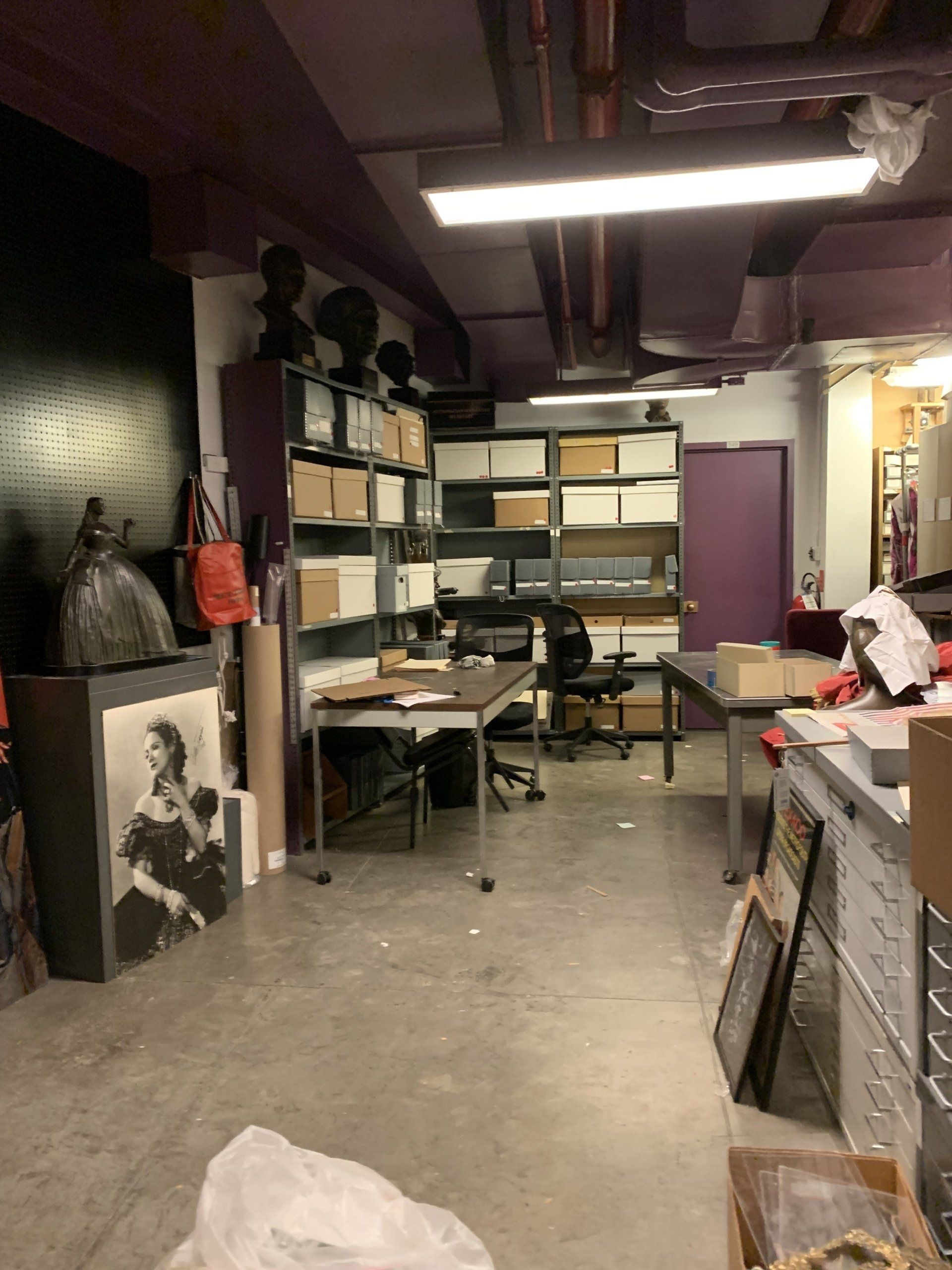 Storage room with shelves of boxes, desk, artwork, and various supplies.