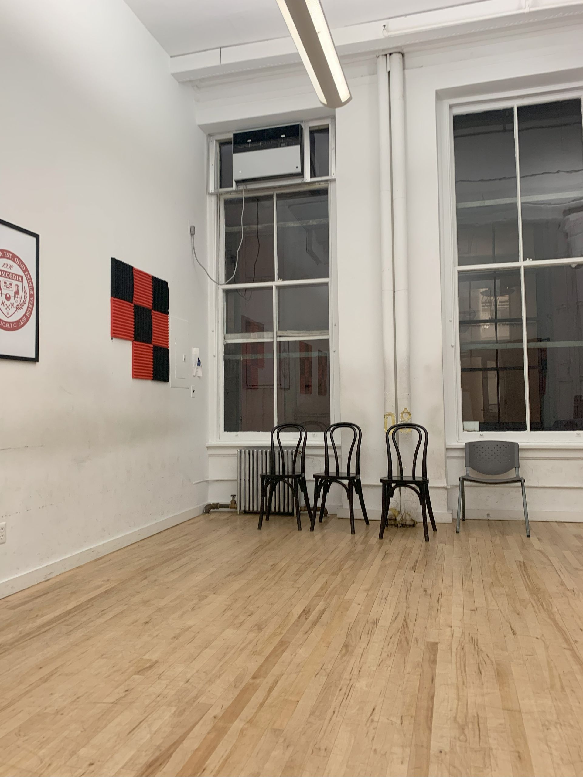 Empty studio with wood floor, white walls, large windows, chairs, and some artwork.