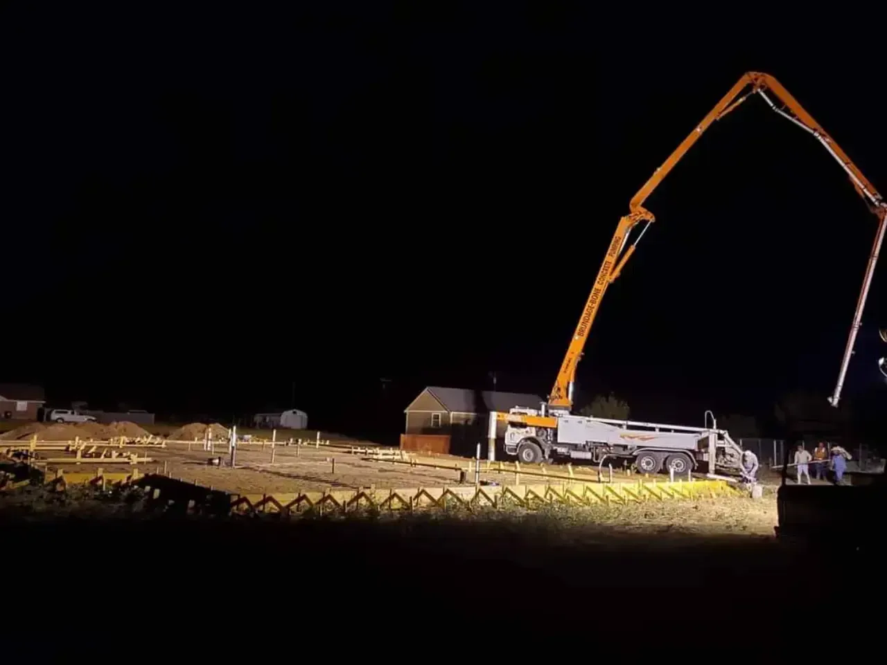 A concrete pump is working on a construction site at night.