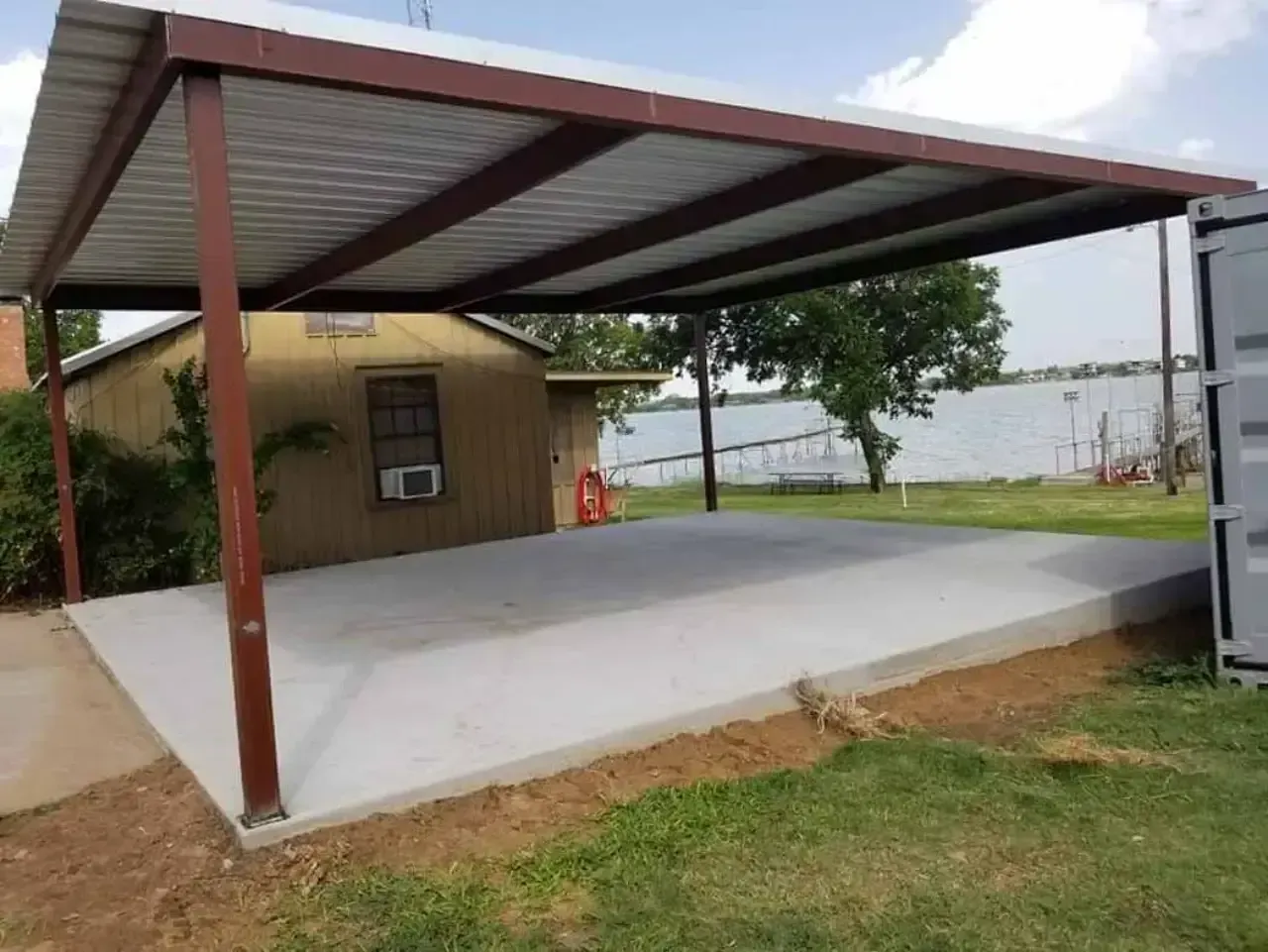 A carport is sitting in front of a house next to a body of water.
