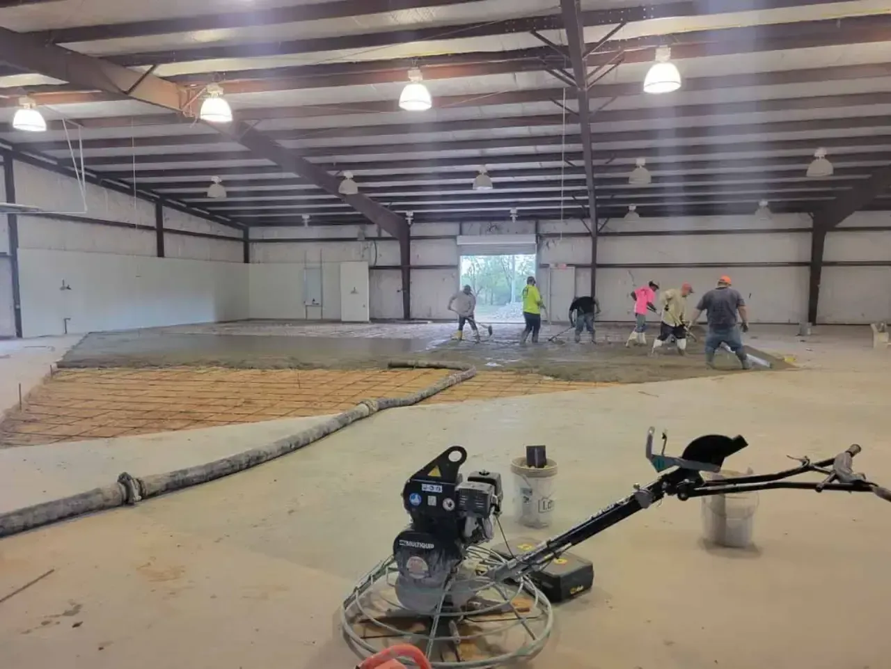A group of people are working on a concrete floor in a large warehouse.