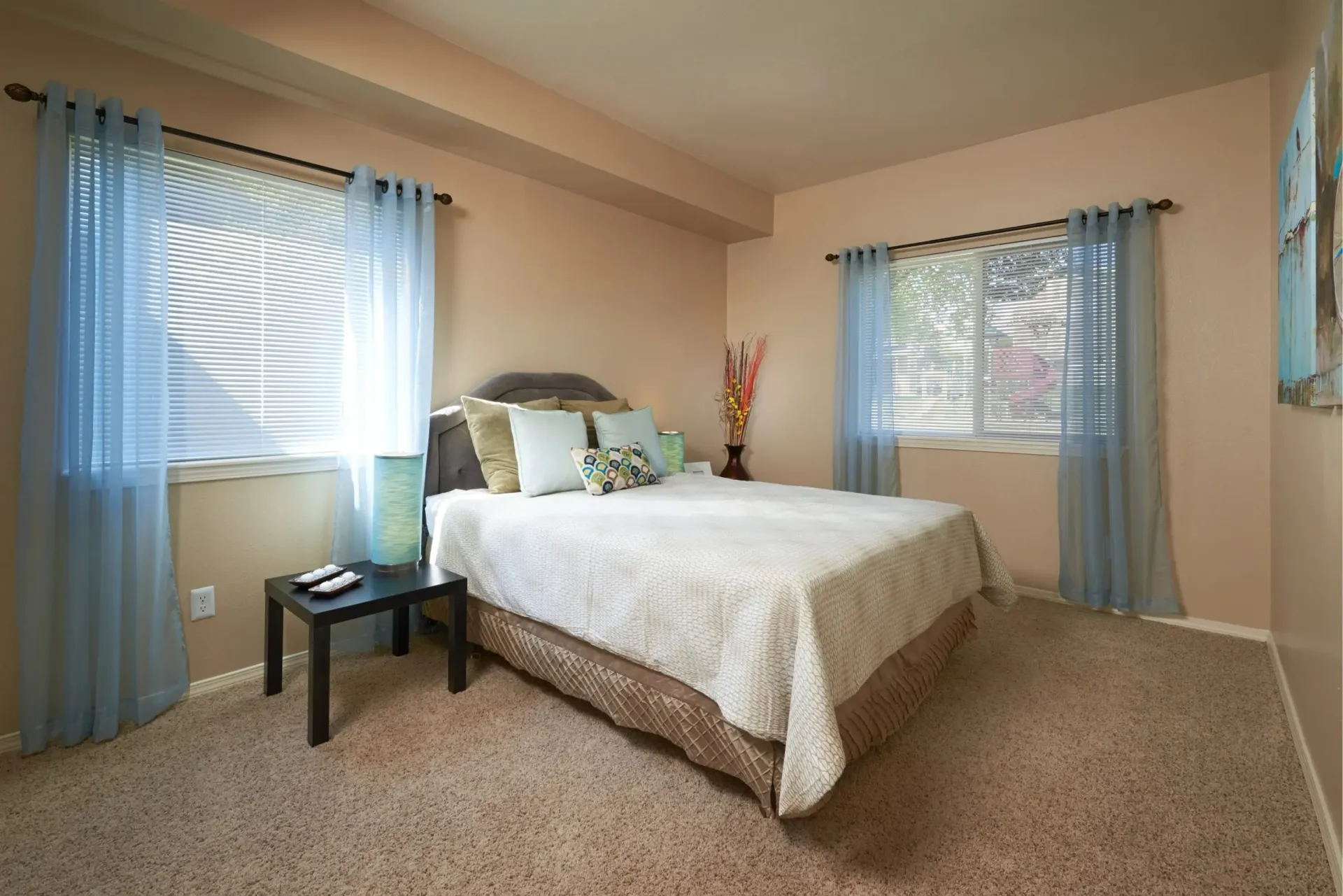 Bedroom with a queen-size bed, blue curtains, and a side table.