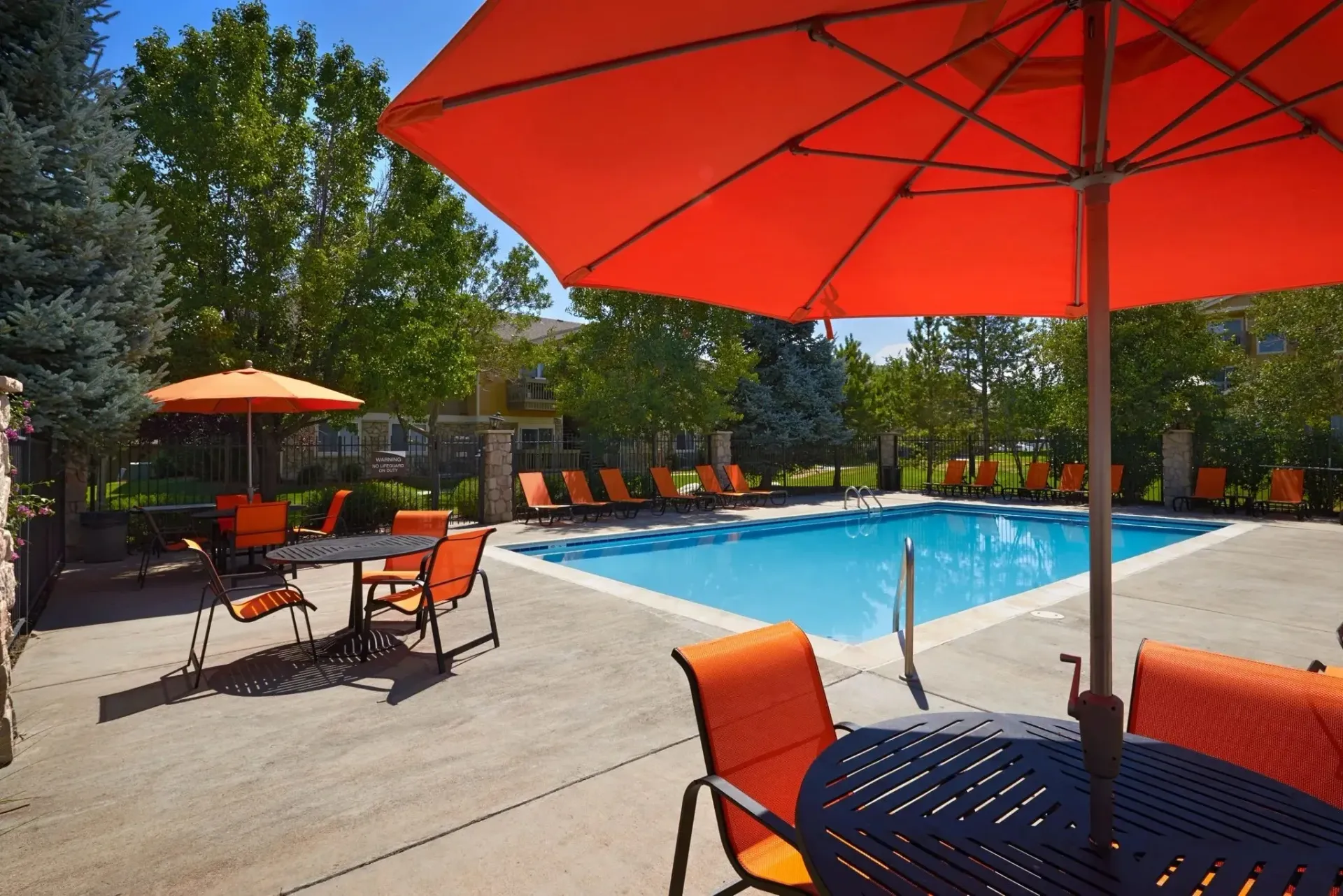 Outdoor swimming pool with lounge chairs and tables under umbrellas.