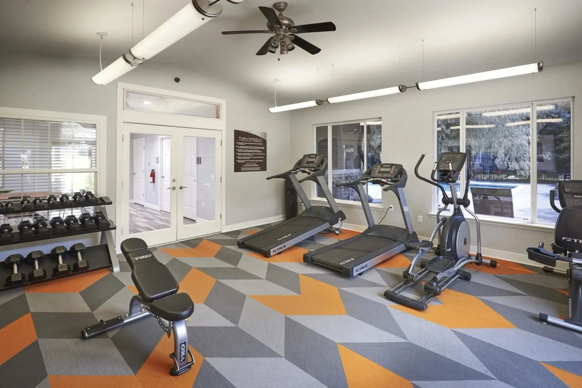 Gym with treadmills, elliptical, weight bench, and dumbbells.
