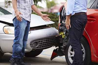 Two men standing near cars with front-end damage, appearing to argue outdoors.