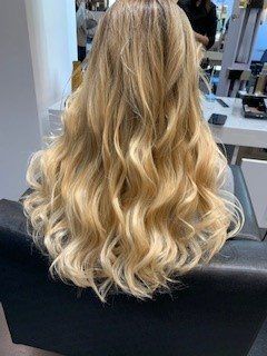 Capelli biondi lunghi e ondulati con mèches, acconciati da dietro in un salone di bellezza.