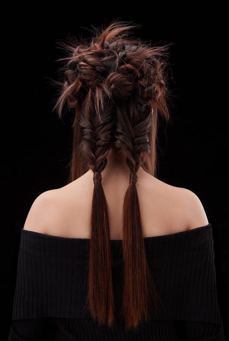 Una persona con i capelli castano scuro raccolti in un'acconciatura disordinata con due lunghe trecce a spina di pesce, che indossa un top nero a spalle scoperte.