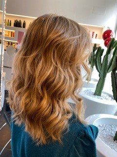 Capelli mossi di media lunghezza, color biondo fragola, in un salone di bellezza, con un cactus verde sullo sfondo.