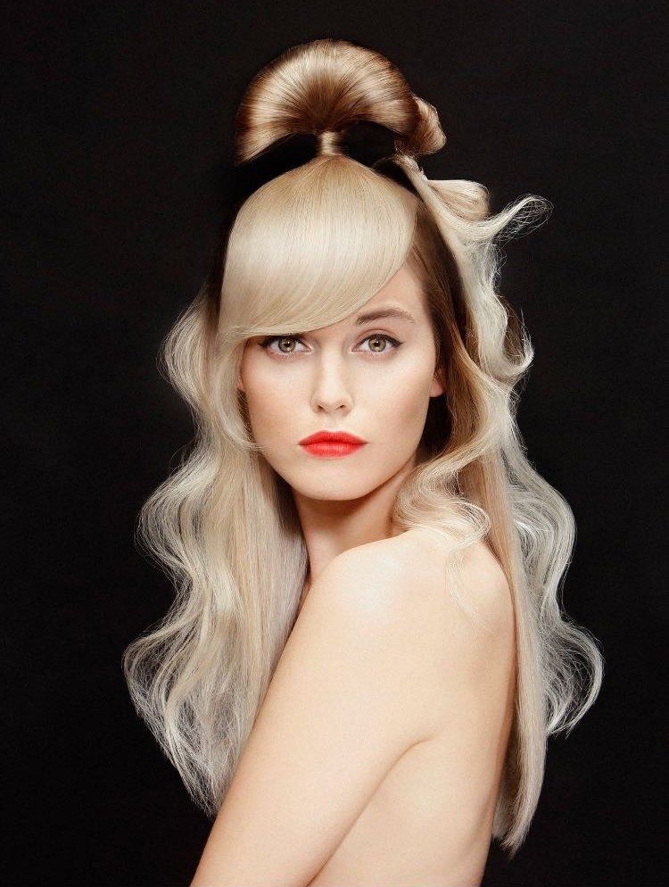 Una persona con i capelli biondo platino raccolti in uno chignon alto con un nastro nero, che indossa un rossetto rosso acceso.