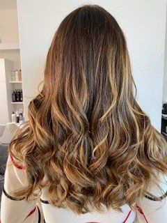 Capelli lunghi, mossi e castani con riflessi color miele, visti da dietro in un salone di bellezza.