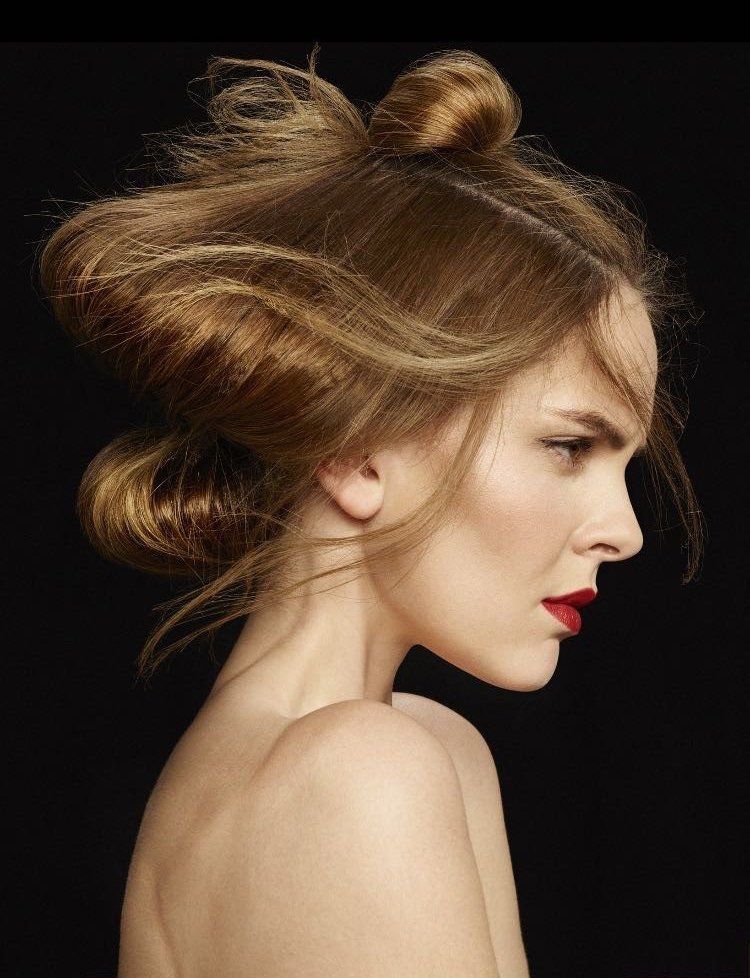 Ritratto di profilo di una persona con capelli castano chiaro raccolti in due chignon, su uno sfondo nero intenso.