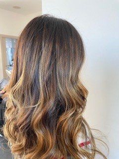 Capelli lunghi e ondulati che sfumano dal castano scuro alle radici al castano dorato chiaro alle punte.