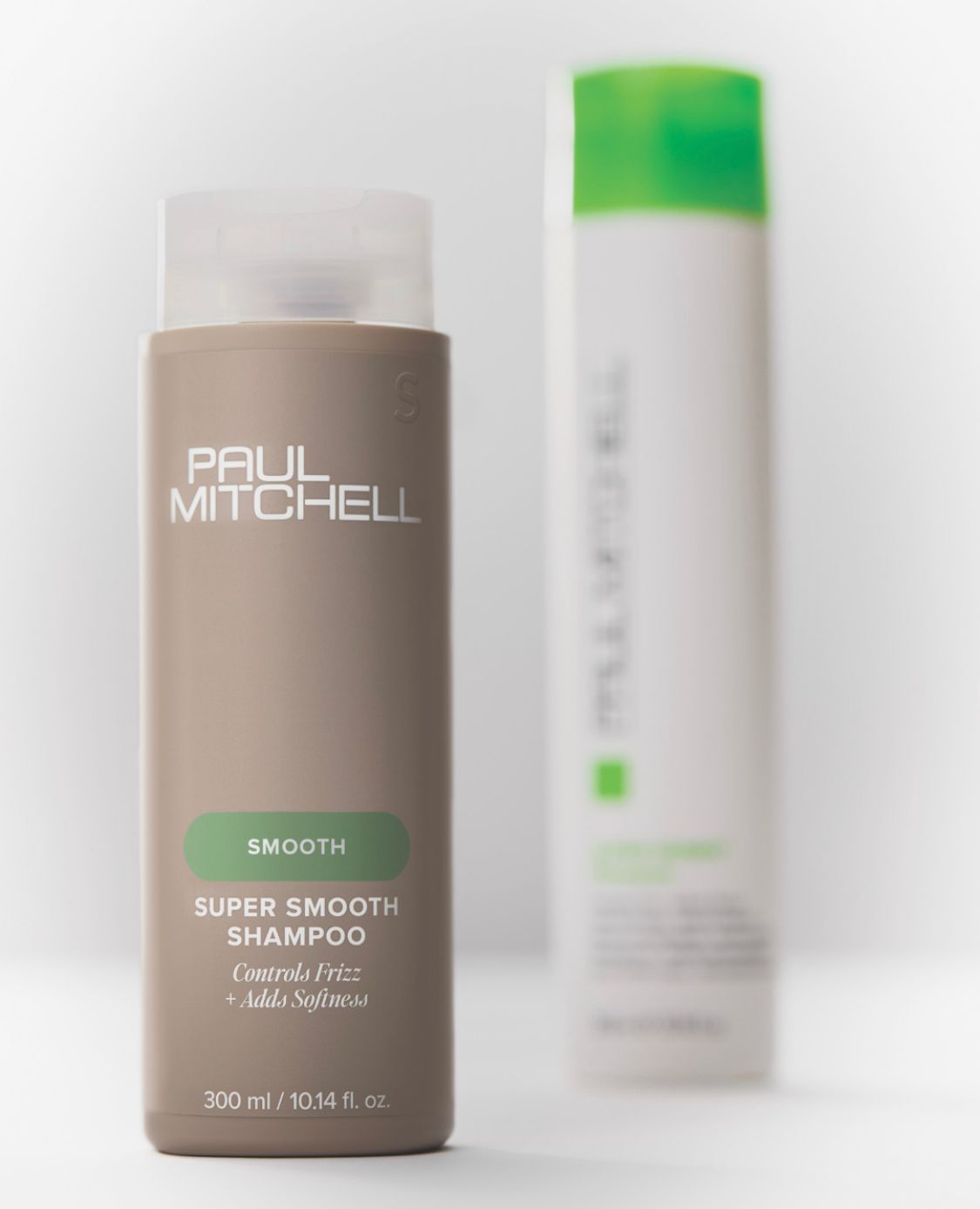 In primo piano, una bottiglia color beige di shampoo Paul Mitchell Super Smooth, con sullo sfondo una bottiglia sfocata bianca e verde.