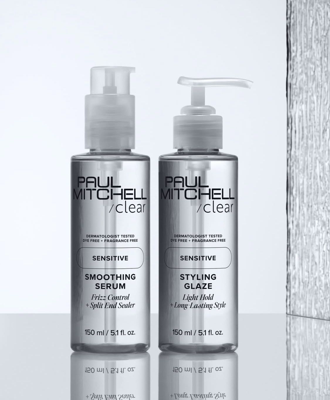 Due flaconi di prodotti per capelli Paul Mitchell Clear, un siero lisciante e un balsamo modellante, sono posizionati su uno sfondo grigio chiaro.