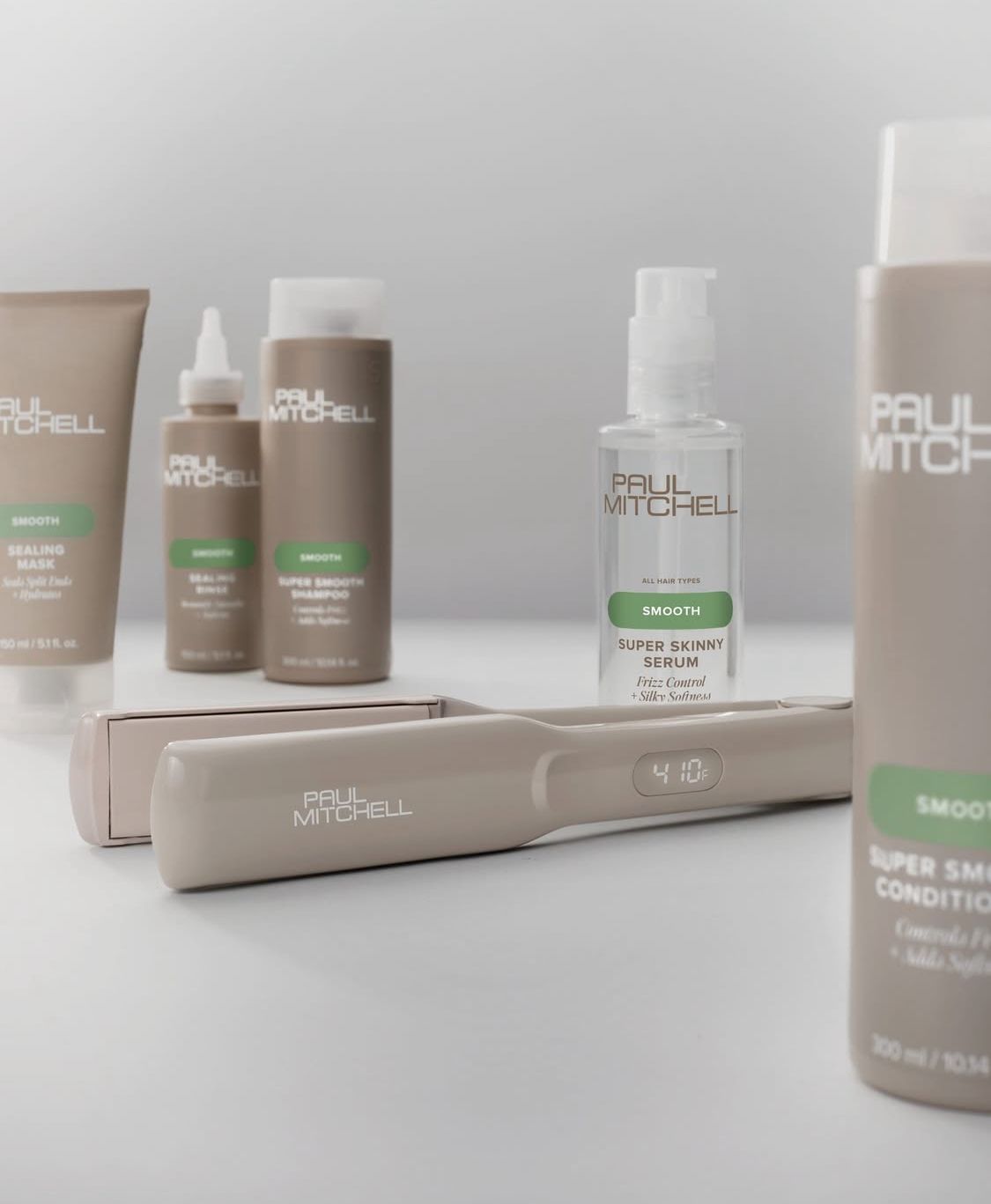 Una collezione di prodotti per la cura dei capelli Paul Mitchell Super Skinny e una piastra per capelli, disposte su uno sfondo neutro.