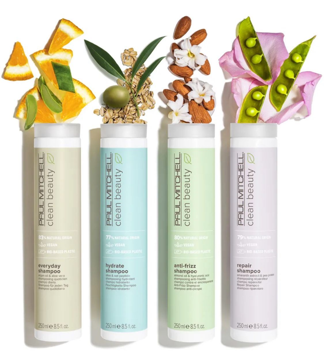 Quattro flaconi di shampoo Paul Mitchell Clean Beauty con ingredienti a base di frutta e fiori che galleggiano sopra ciascuno di essi.
