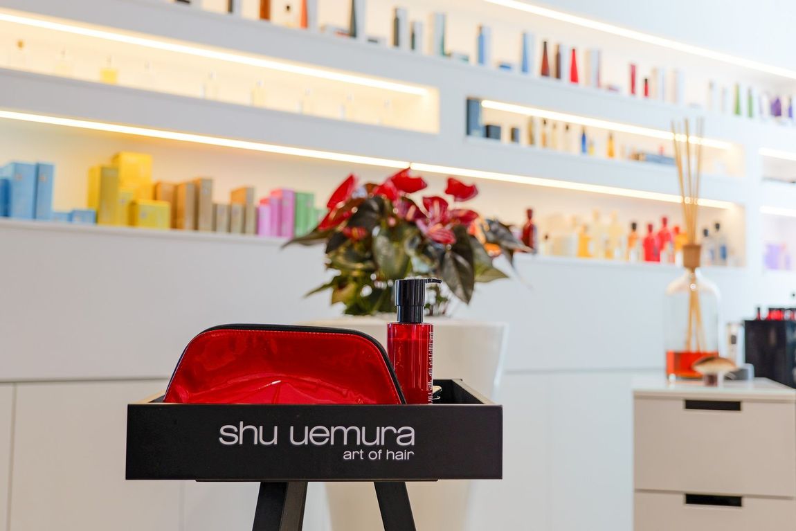 Un kit per lo styling dei capelli ghd rosso su un supporto nero in un moderno salone di parrucchieri con sedie nere e scaffali pieni di prodotti di bellezza.