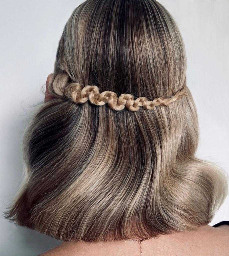 Una persona con capelli di media lunghezza, ondulati, acconciati con una treccia orizzontale a spirale che attraversa la parte posteriore della testa.