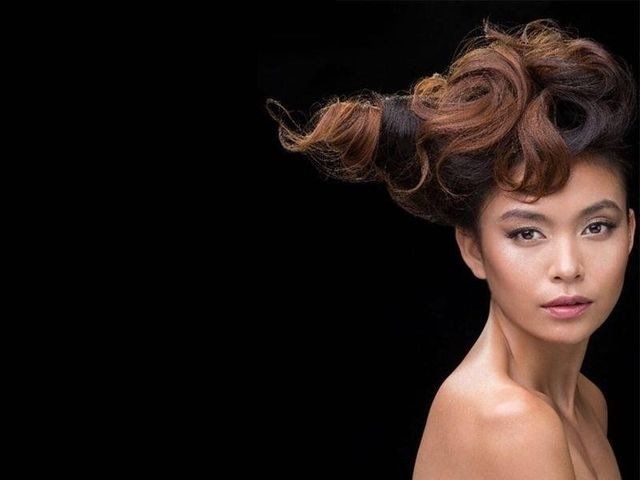 Una persona con capelli castani e neri, voluminosi e ben definiti, su sfondo nero.