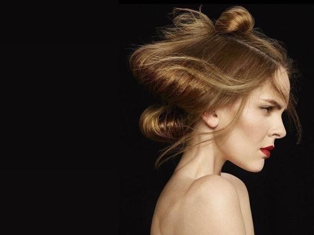 Ritratto di profilo di una persona con un'acconciatura a più chignon e un rossetto rosso acceso, su sfondo nero.