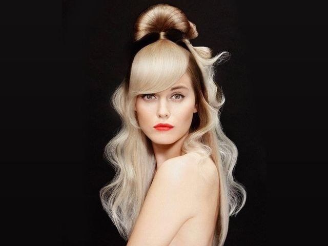 Modella con capelli biondo platino raccolti in uno chignon semi-raccolto e morbide onde, con indosso una fascia nera, su sfondo nero.