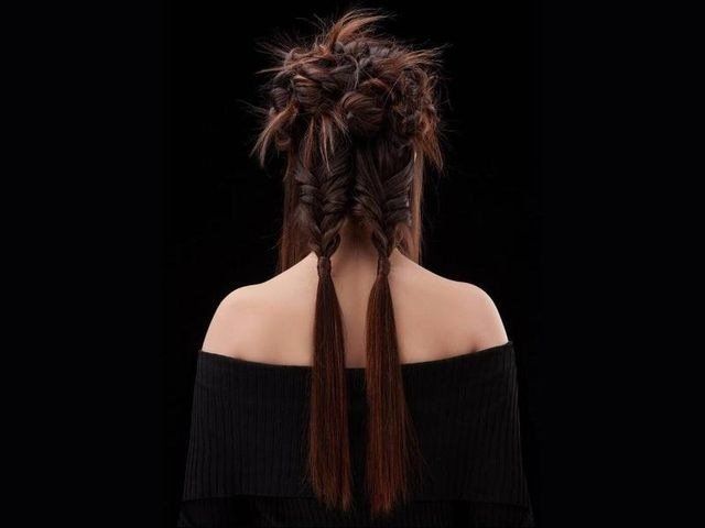 Una persona con lunghi capelli castani acconciati in due trecce disordinate e texturizzate che terminano con ciocche morbide e fluenti su uno sfondo nero.