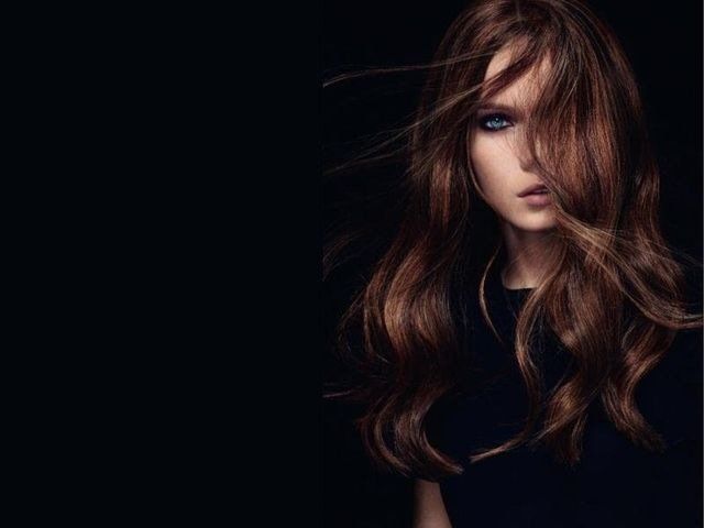 Una persona con lunghi capelli castani fluenti che le coprono parte del viso, su uno sfondo scuro e minimalista.