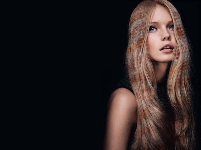 Una persona con lunghi capelli biondi ondulati e mèches arricciate e texturizzate su uno sfondo nero uniforme.