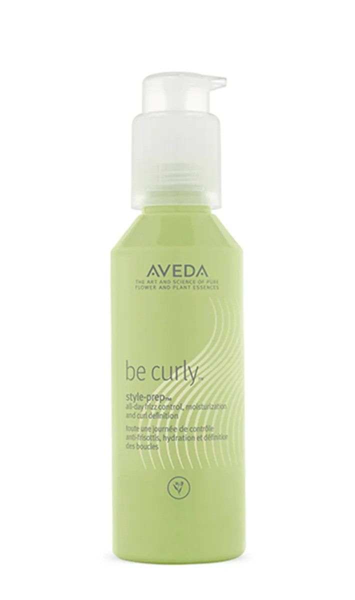 Una bottiglia verde chiaro di siero per capelli ricci Aveda Be Curly con dosatore a pompa bianco su sfondo bianco.