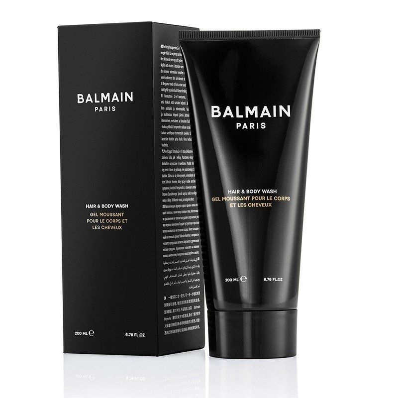 Un tubetto nero di detergente per capelli e corpo Balmain Paris accanto alla sua scatola nera abbinata, su una superficie bianca.